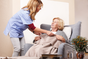 portrait of smiling elderly woman sitting at home in living room and accepts a blanket given by her caregiver