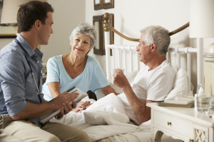 portrait of smiling elderly man on bed with his wife and caregiver